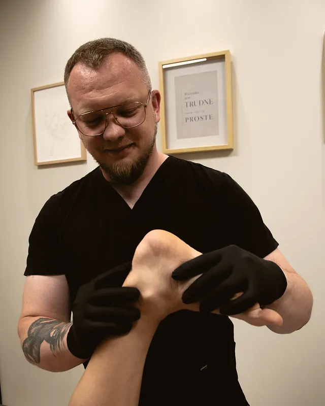 Fizjoterapeuta Marcin Jędrzejewski bada dłońmi piętę i stopę pacjenta w gabinecie RH Fizjo w Koninie